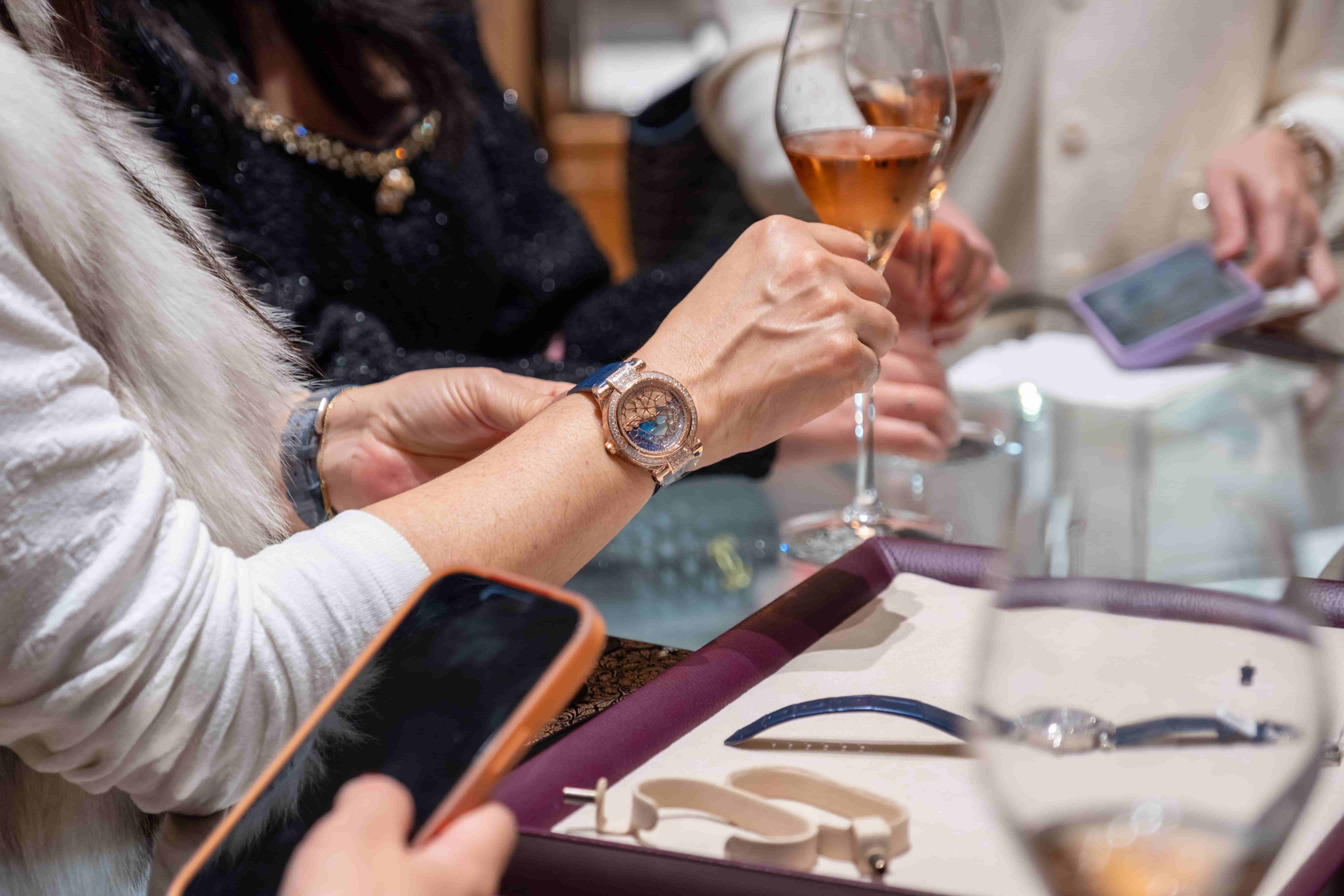 A guest trying on a Chopard Imperiale watch with a blue dial, holding a glass of Krug champagne at a boutique event.