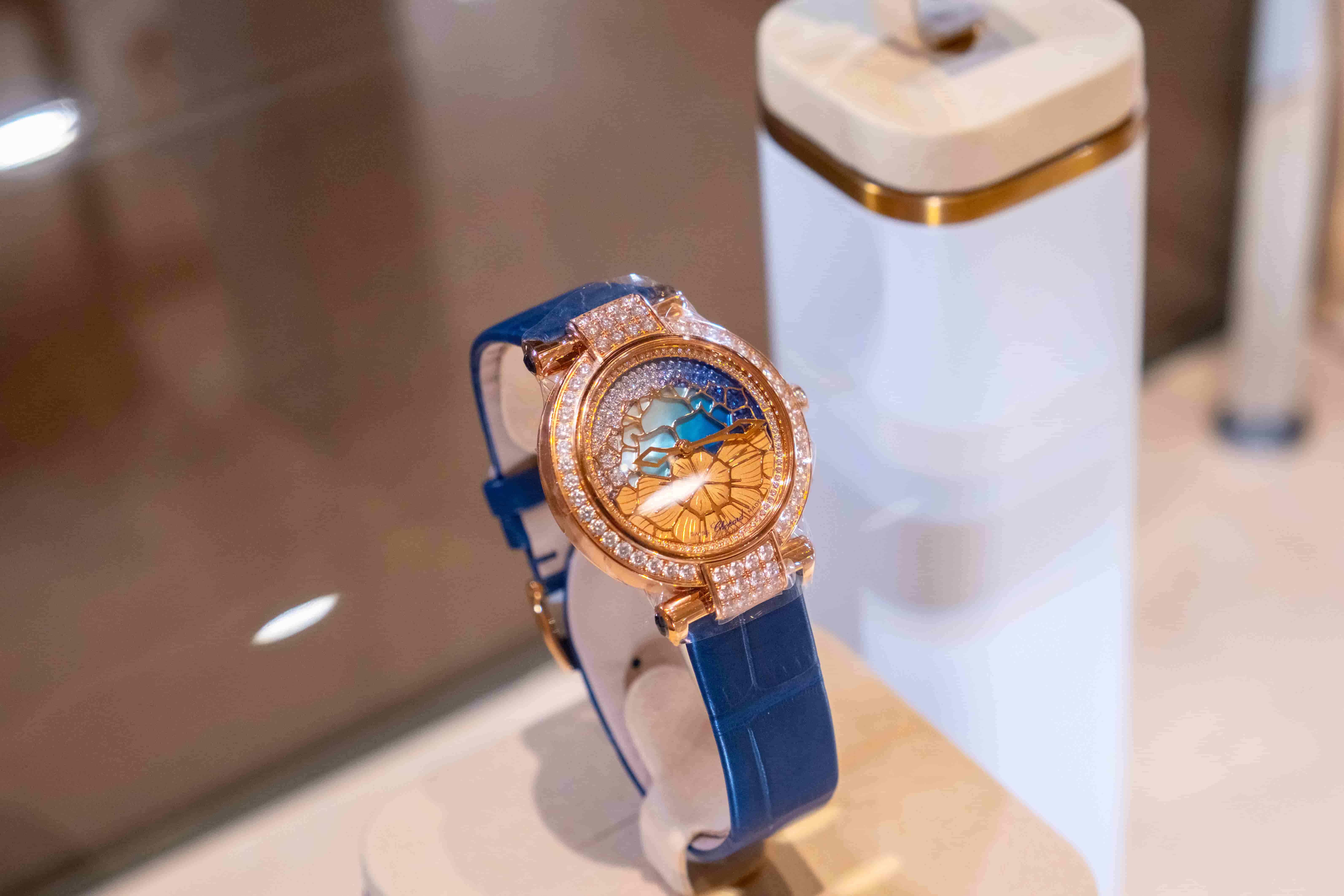 Close-up of a Chopard Imperiale watch with an intricate gold and blue lace-patterned dial, showcasing the diamond bezel and blue leather strap.
