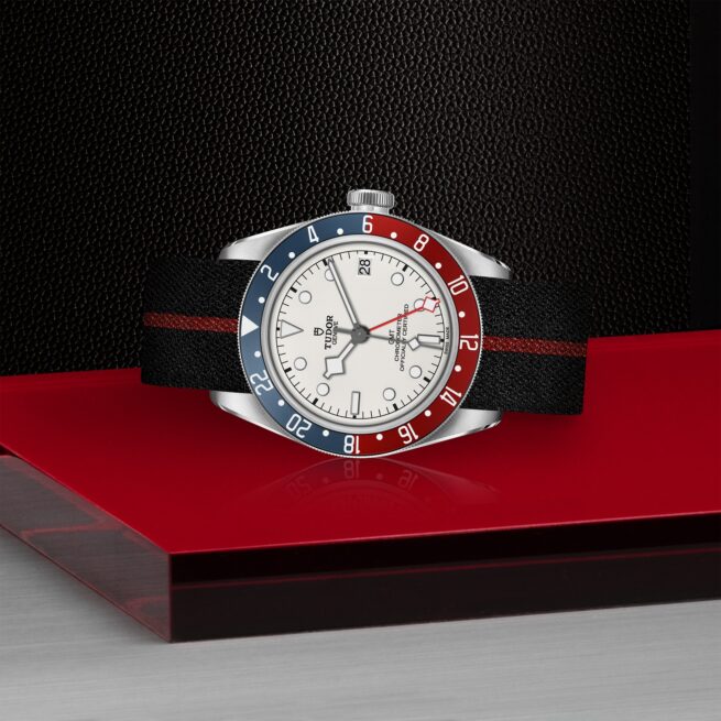 A M79830RB-0012 watch sits on a red table.