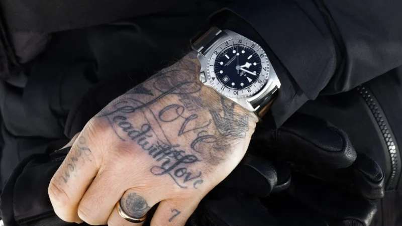 A man with tattoos on his wrist wearing a tudor watch.