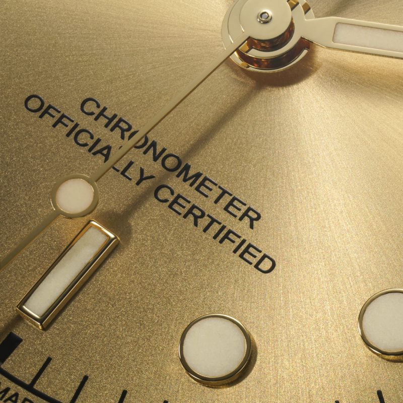 Close-up view of a gold watch face showing the words "Chronometer Officially Certified" along with the hands and markers of the M79643-0005.