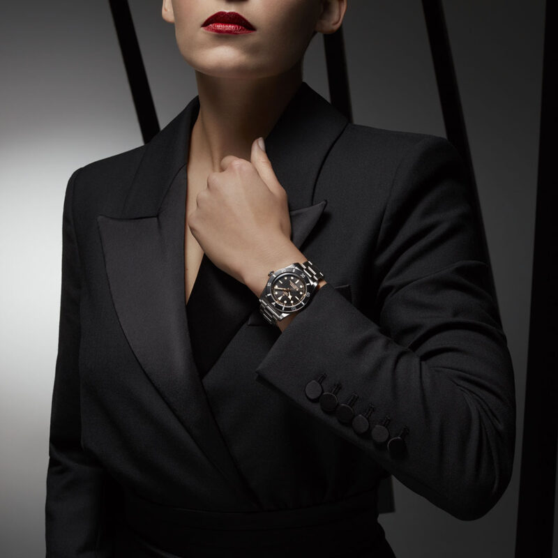 A woman in a black suit wearing a M79000N-0001 watch.