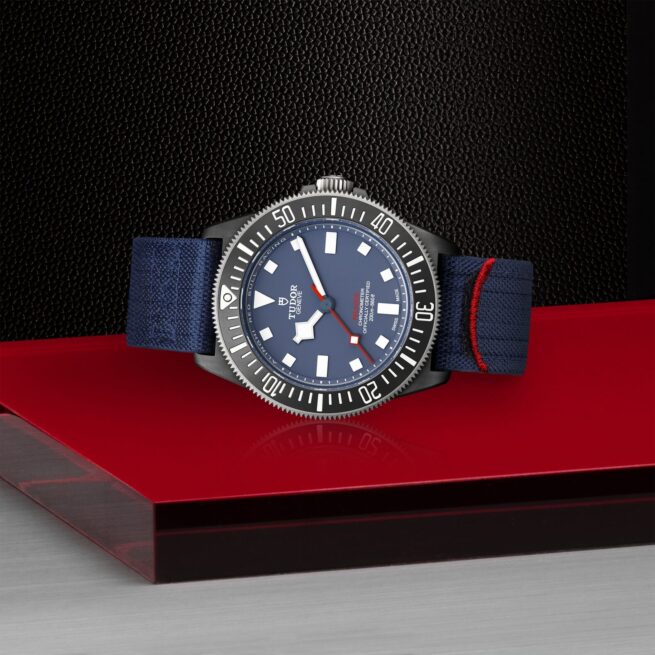 A M25707KN-0001 with a blue strap sitting on a red surface.