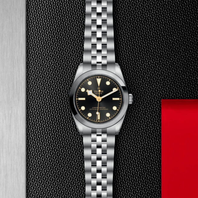 A M79600-0001 watch with a black dial on a red background.