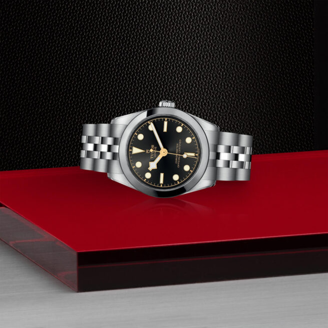 A M79600-0001 watch with a black dial on a red table.