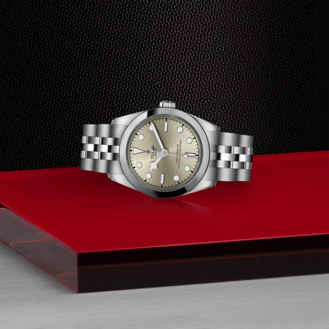 A silver M79600-0003 watch sitting on a red table.