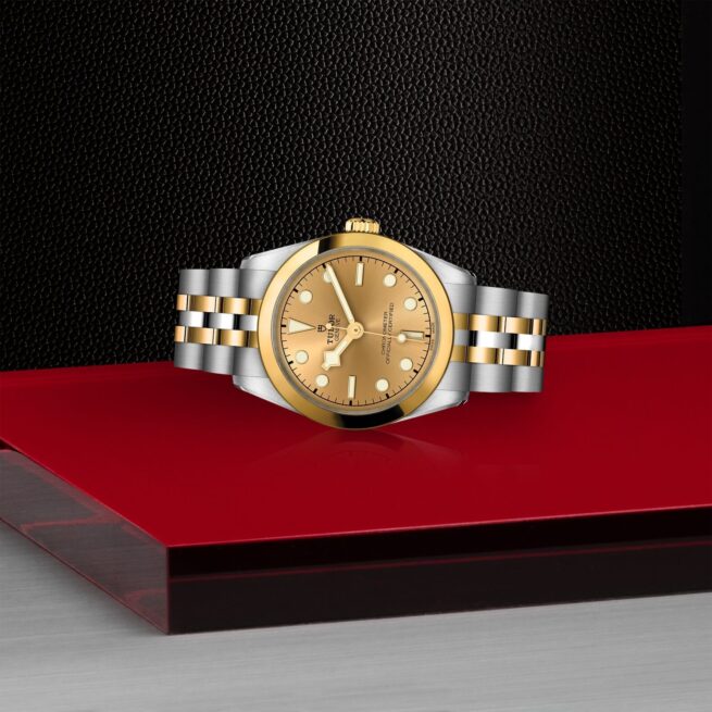 A gold and yellow M79603-0005 watch on a red table.