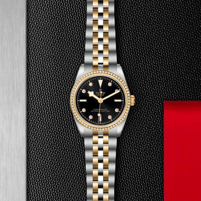 A black and gold M79613-0005 watch on a red background.