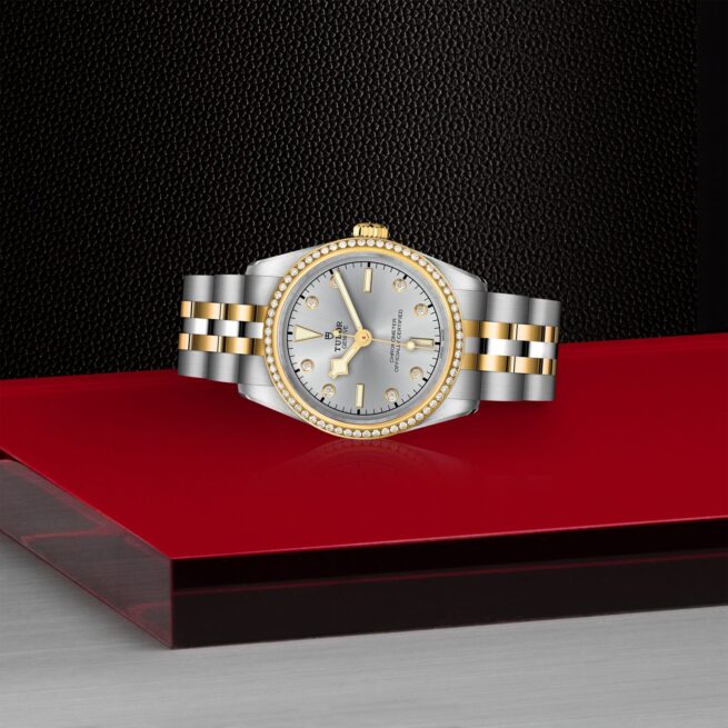 The M79613-0006 ladies watch is displayed on a red table.