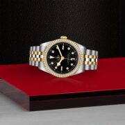 A M79653-0005 watch with a black dial on a red table.
