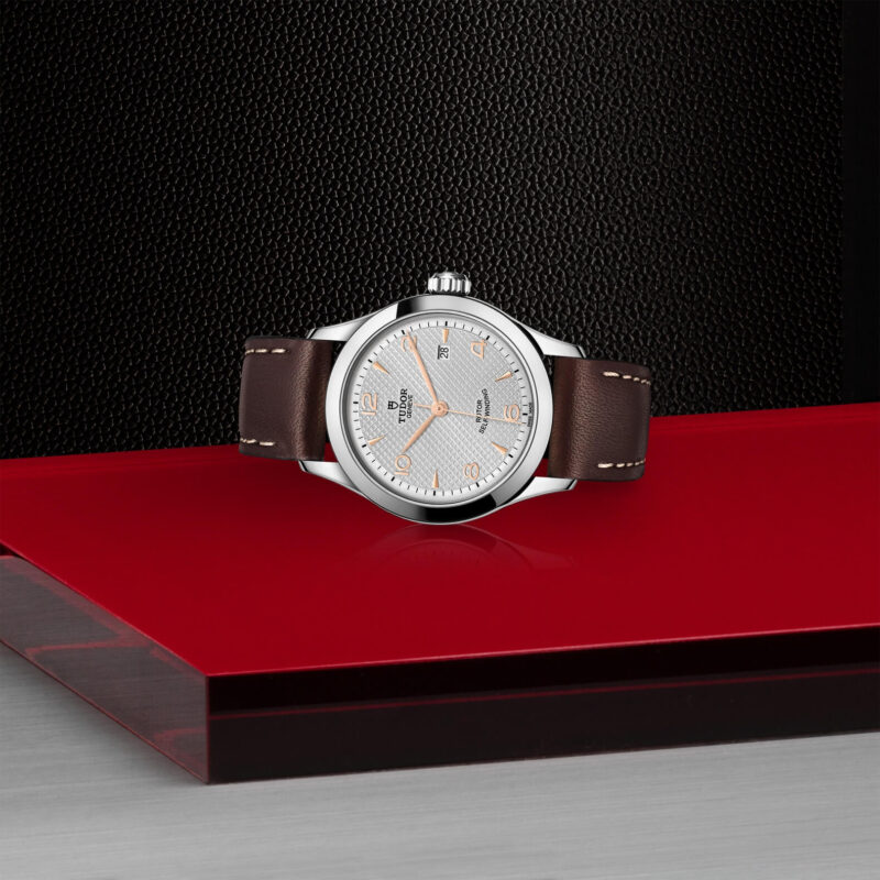 A watch with a M91350-0006 strap sitting on a red table.