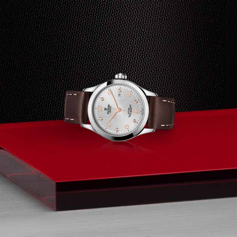 A M91350-0007 with a brown leather strap sitting on a red surface.