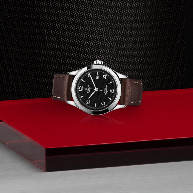 A M91350-0008 with a brown leather strap sitting on a red surface.