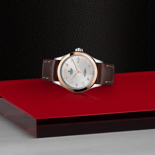 M91351-0006 with a brown leather strap sitting on a red table.