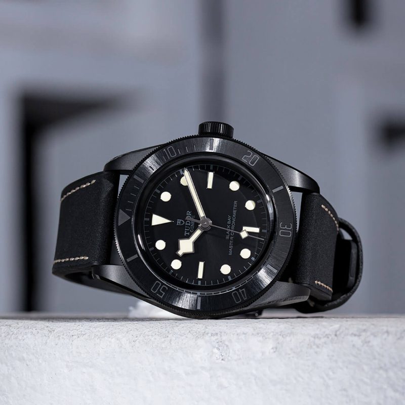 A black M79210CNU-0001 watch sitting on a concrete wall.