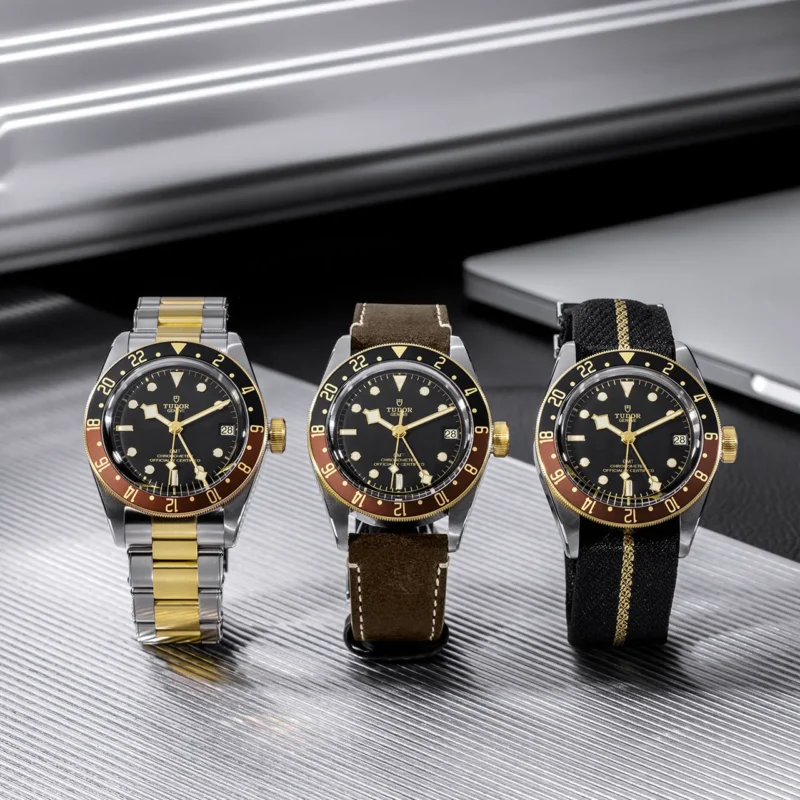 Three M79833MN-0003 watches with gold and black dials sitting on a table.