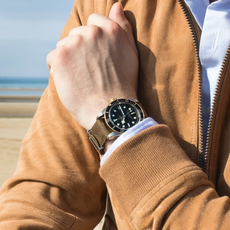 A man in a brown jacket is wearing a M79733N-0005 on the beach.