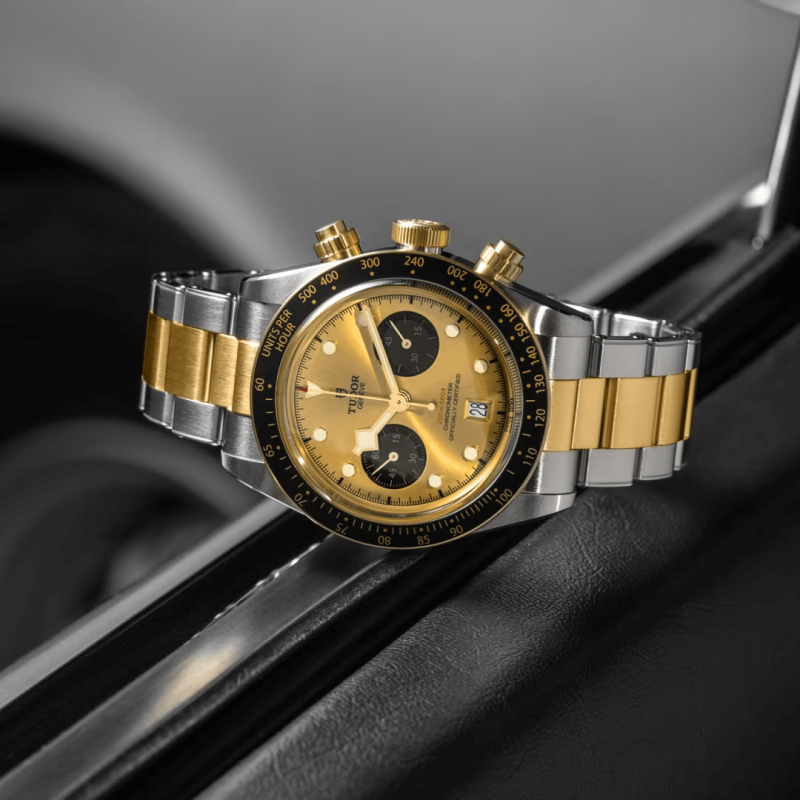 A M79363N-0007 with a silver and gold band and a gold face with black subdials, positioned on a reflective surface.