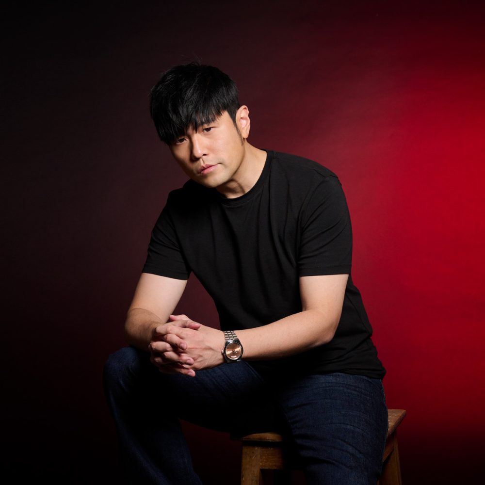 A man in a black shirt sitting on a stool.