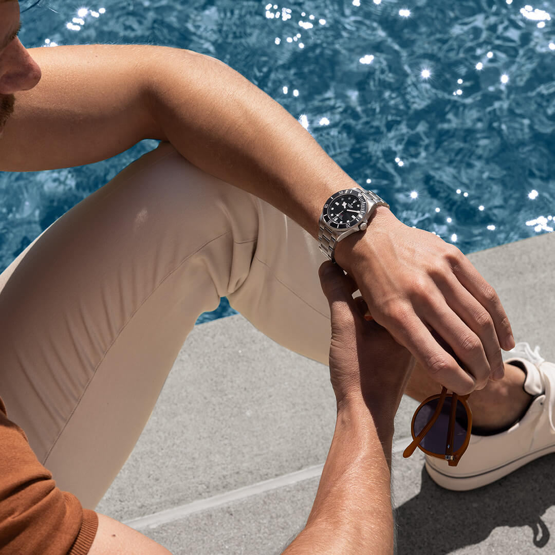 A man is putting on a watch next to a pool.