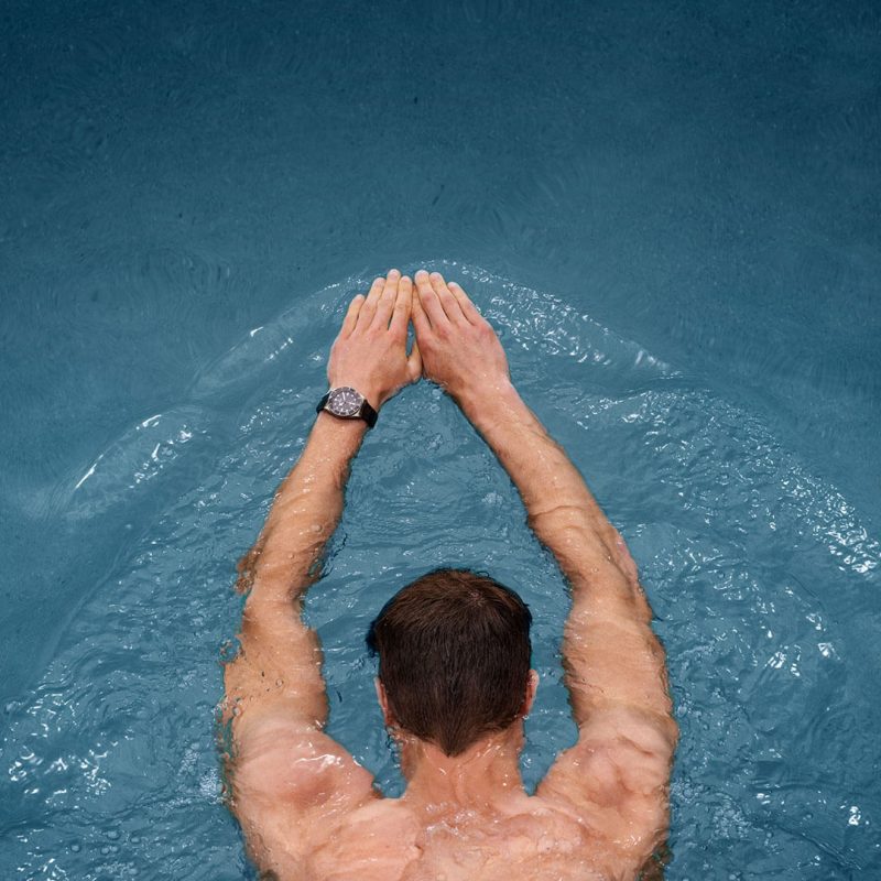 A man in a swimming pool with his hands raised in the air.