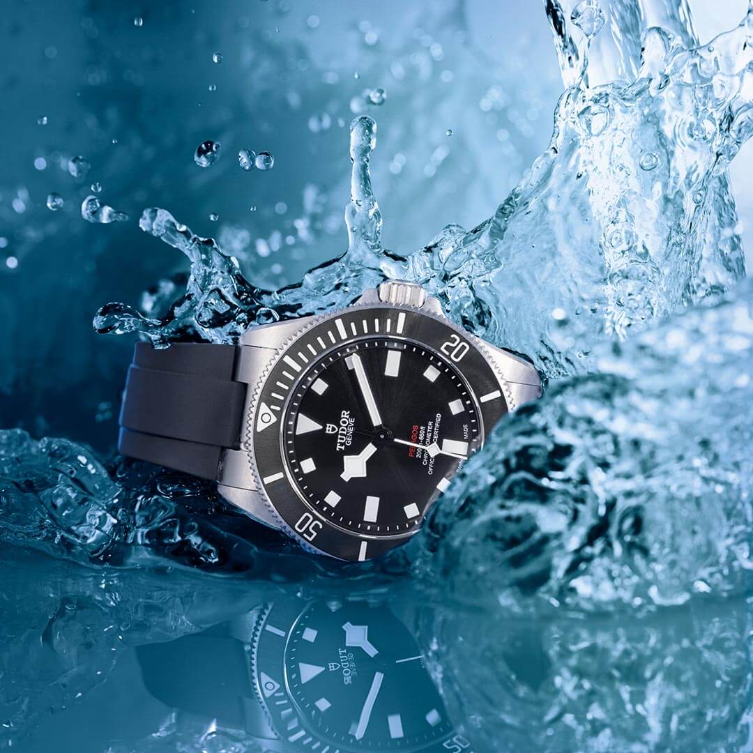 A tudor watch in the water with water splashing on it.