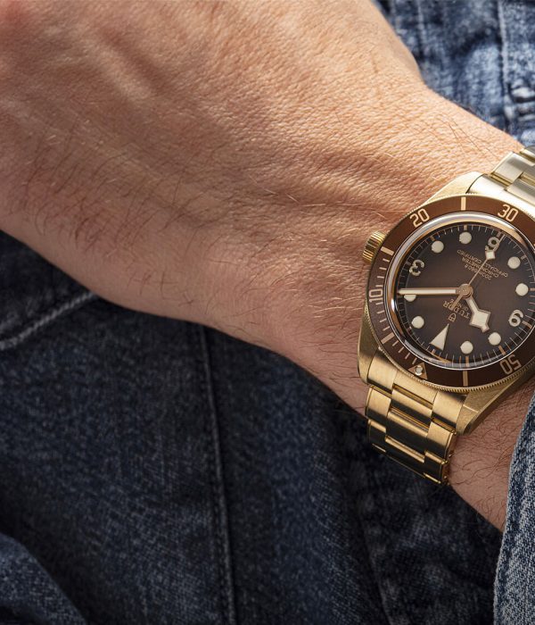 A man is wearing a gold tudor watch on his wrist.