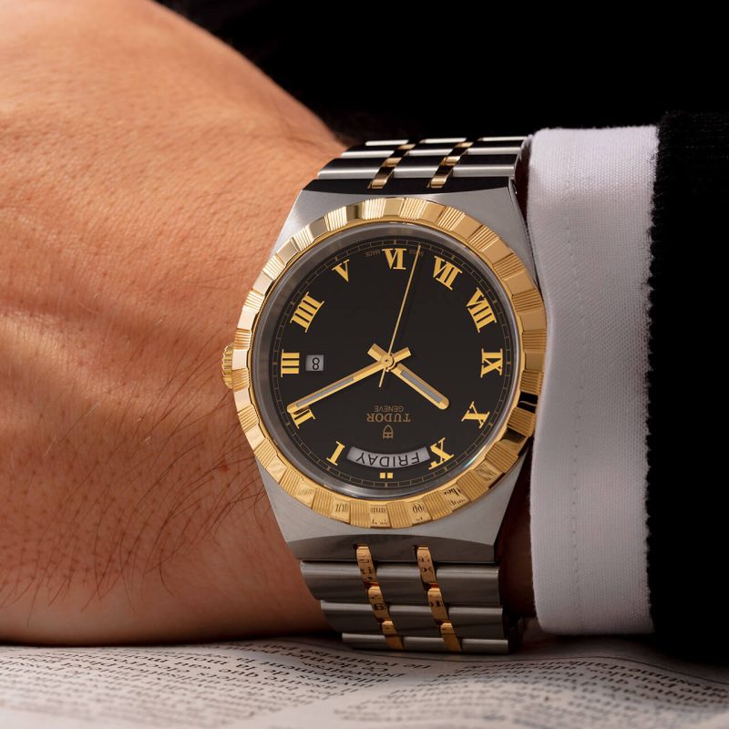 A man wearing a gold and black watch with roman numerals.