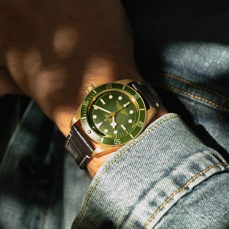 A person wearing a watch with a green dial.