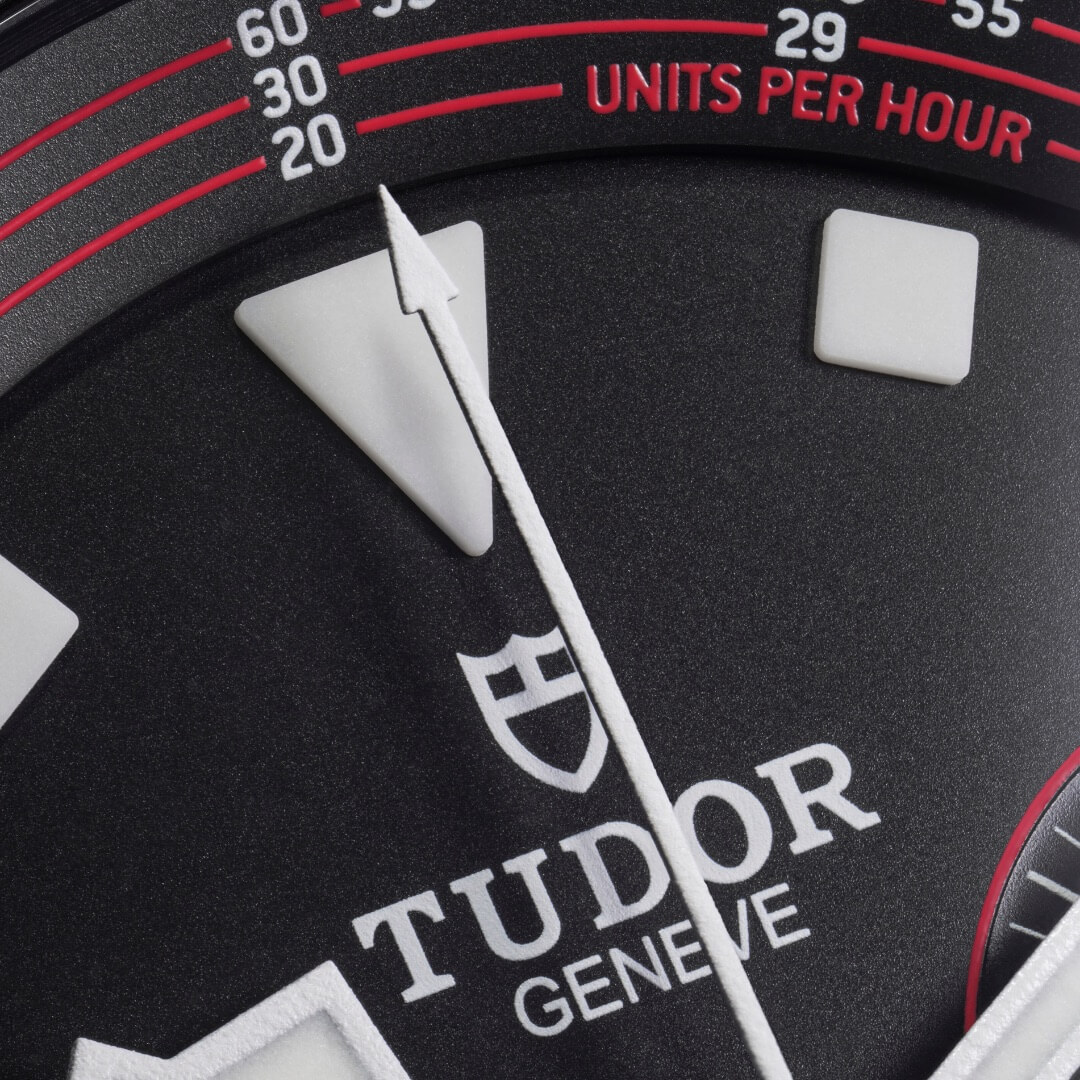 Close-up of a Tudor M25827KN-0001 watch face showing the brand's logo, "TUDOR GENEVE," with various time markings and a white arrow-shaped minute hand pointing at the 20-minute mark.