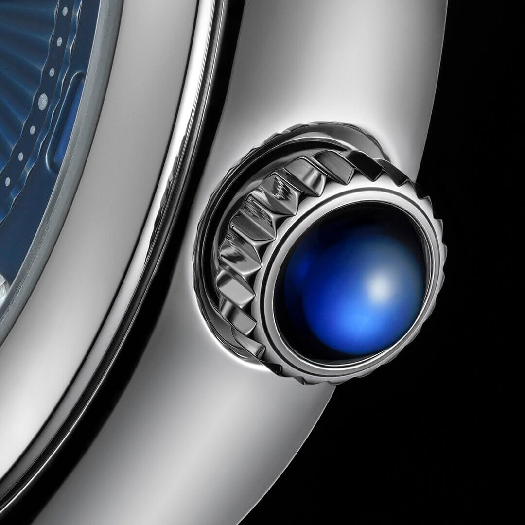 Close-up view of a metallic watch crown with a blue cabochon gemstone, attached to the M35800-0010 casing.