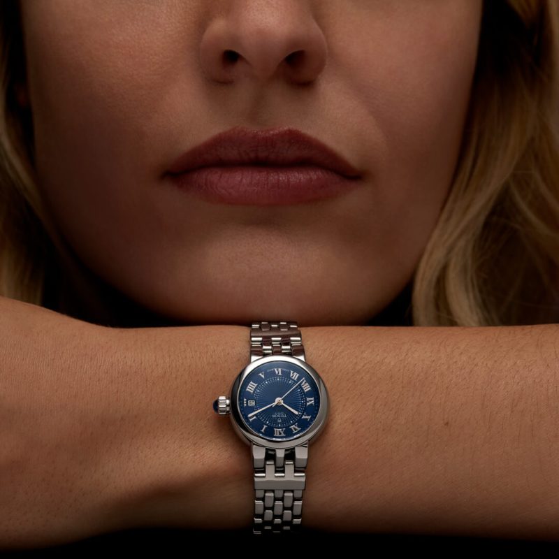 A person rests their chin on their arm, displaying a M35800-0010 with a blue dial and Roman numerals.