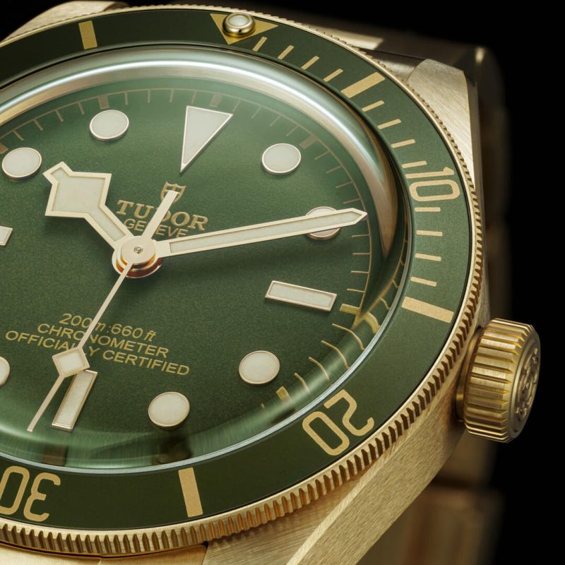 Close-up of a M79018V-0006 watch featuring a green bezel and dial, gold-tone case, and indices, displaying time with hour, minute, second hands, and a 60-minute marker ring.