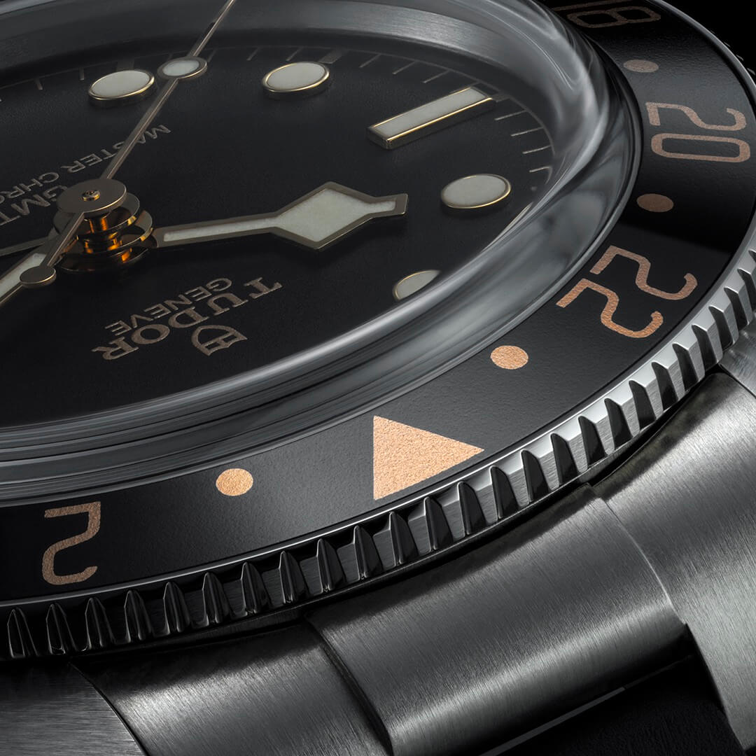 Close-up of a wristwatch featuring a black dial with luminescent hands and markers, a domed crystal, and a stainless steel bracelet. The watch displays the product name "M7939G1A0NRU-0001" on the dial.