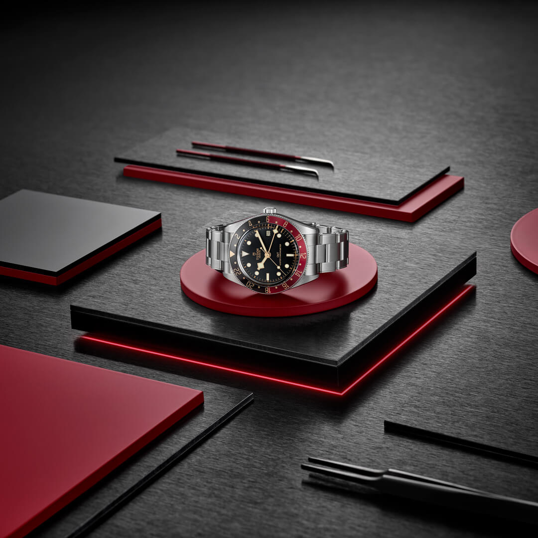 A M7939G1A0NRU-0001 with a black dial and red accents is displayed on a red and black platform with geometric shapes in the background.