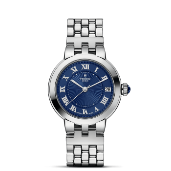 A silver wristwatch with a blue dial featuring Roman numerals and a date display, labeled "Tudor" below the 12 o'clock mark, against a black background.