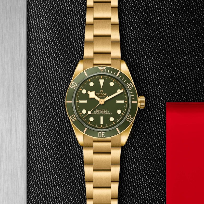 A gold wristwatch with a green face and bezel, featuring a gold bracelet, is displayed against a textured black background with a red accent.