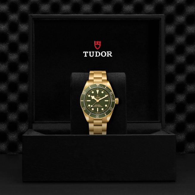 A gold Tudor wristwatch with a green dial displayed in an open black box with the Tudor logo.