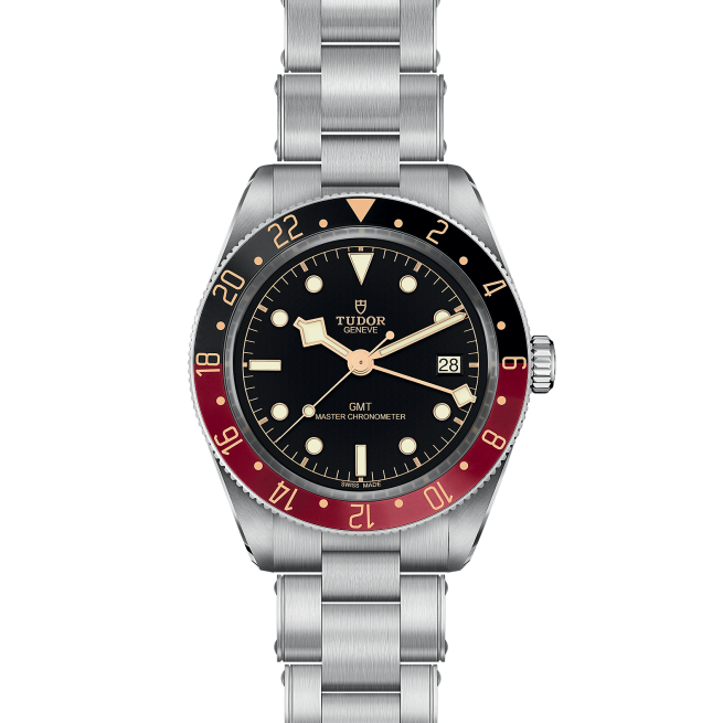 A silver wristwatch with a black dial, red and black bezel, and metal link band. The text on the watch face reads "Tudor Genève GMT Master Chronometer." The watch also displays the date. Product Name: M7939G1A0NRU-0001