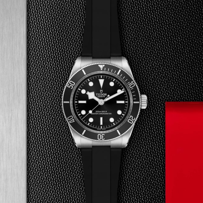 A stainless steel dive watch with a black dial and white markers is displayed on a textured black surface, alongside a red-accented section and a metallic edge.