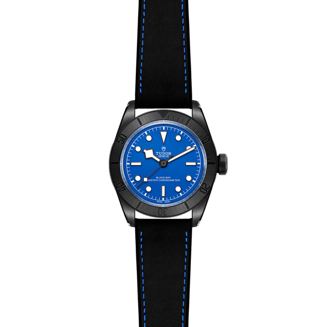 A black Tudor wristwatch with a blue dial, white hour markers, and blue stitching on a black strap, displayed against a black background.