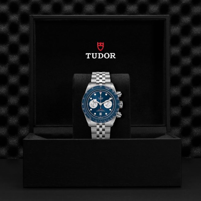 A Tudor wristwatch with a blue dial and silver bracelet displayed inside a black box with the Tudor logo on the lid.