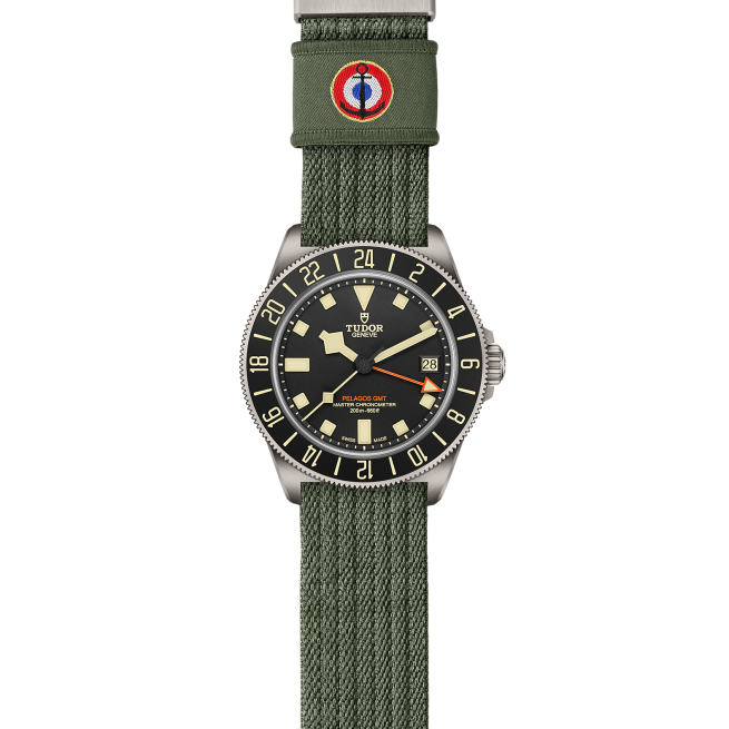 The Tudor Pelagos FXD GMT watch features a black dial with off-white hour markers, and is complemented by an olive green textile strap.