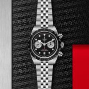The M79360N-0013 is a stainless steel wristwatch featuring a black dial with three subdials, a date display at 6 o'clock, and a textured black background accented with red.