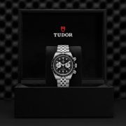 A luxury watch, model M79360N-0013, featuring a stainless steel bracelet and black dial is showcased in a black box labeled "Tudor.