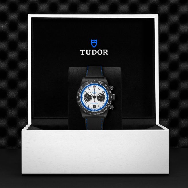 The Tudor M79360B-0002 wristwatch with a blue and white dial is displayed upright in an open white presentation box with a black interior and the Tudor logo.