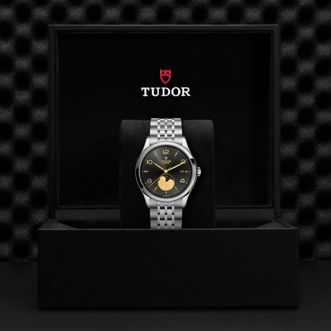 The Tudor M91560-0003 wristwatch with a black dial and moon phase display comes in a black Tudor-branded box.