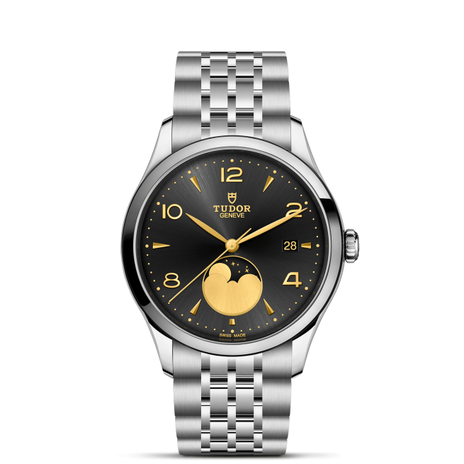 The Tudor M91560-0003 is a silver wristwatch with a black dial, gold hands and accents, a date display at 3 o'clock, and a moonphase complication above 6 o'clock.