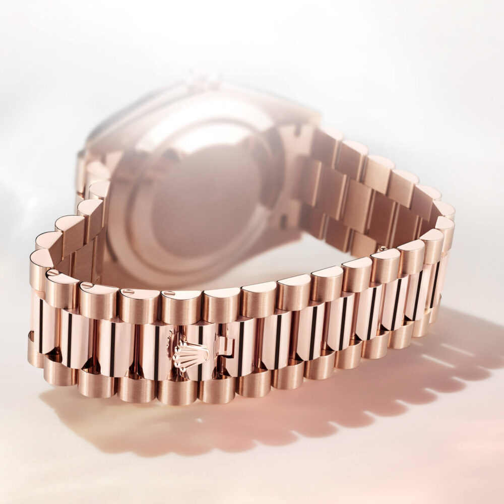 A rose gold wristwatch with a linked bracelet and a clasp featuring a horse logo, displayed on a reflective surface.
