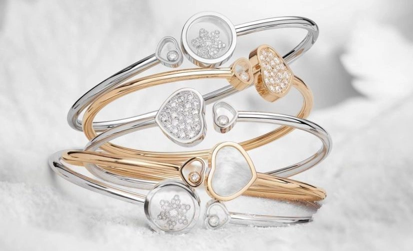 A collection of elegant bracelets in gold and silver, featuring intricate designs with embedded diamonds and pearls on a soft, snowy background.